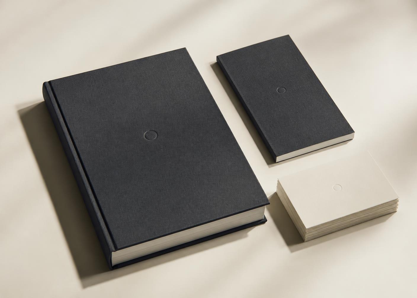 A charcoal linen-bound archival volume beside a second volume and a stack of archival cards